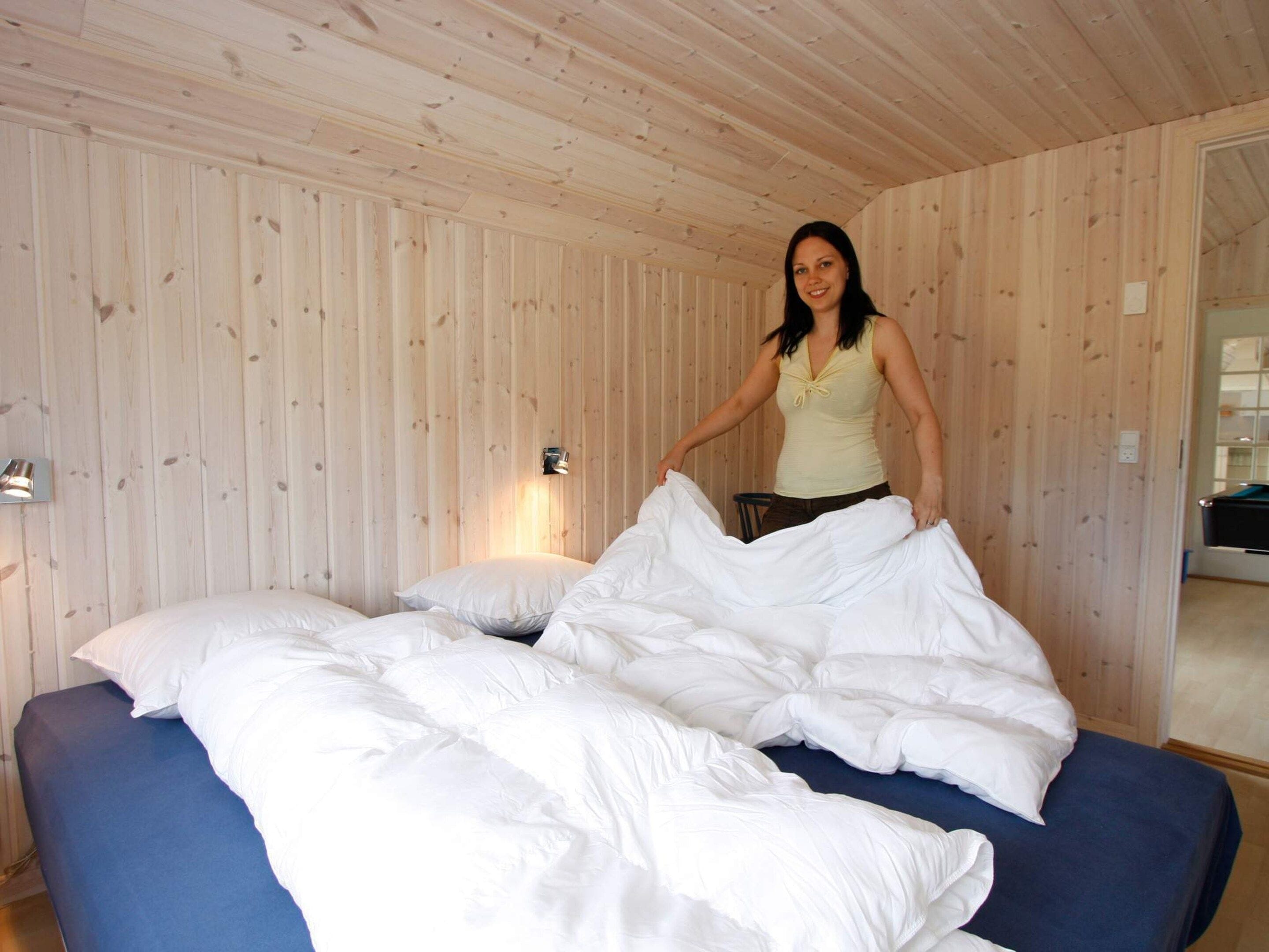 A room with wooden panel walls, a bed with white bedding, and a wall-mounted light fixture.
