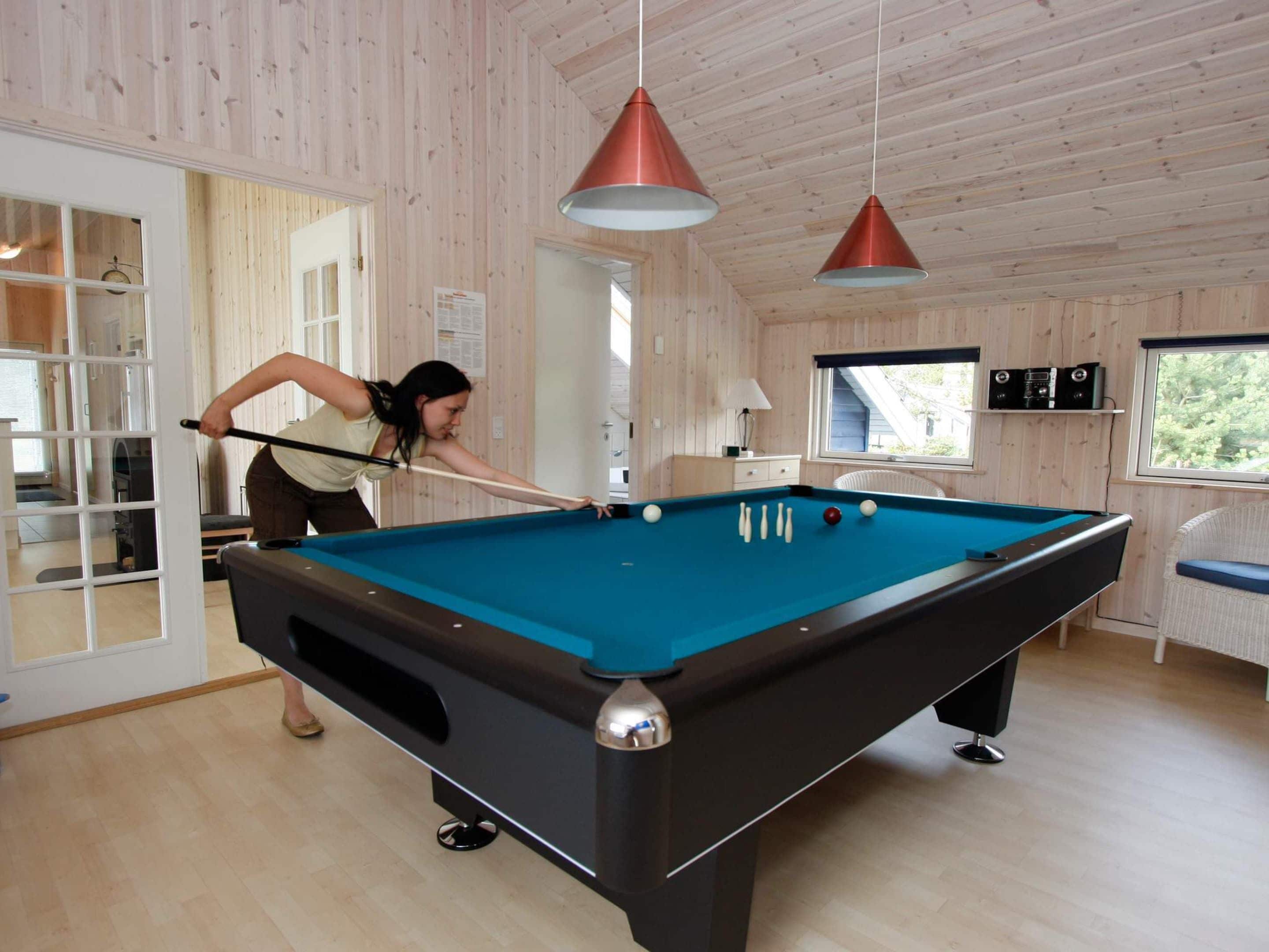 A pool table in a room with wooden walls and ceiling, a door leading outside, and two pendant lights.