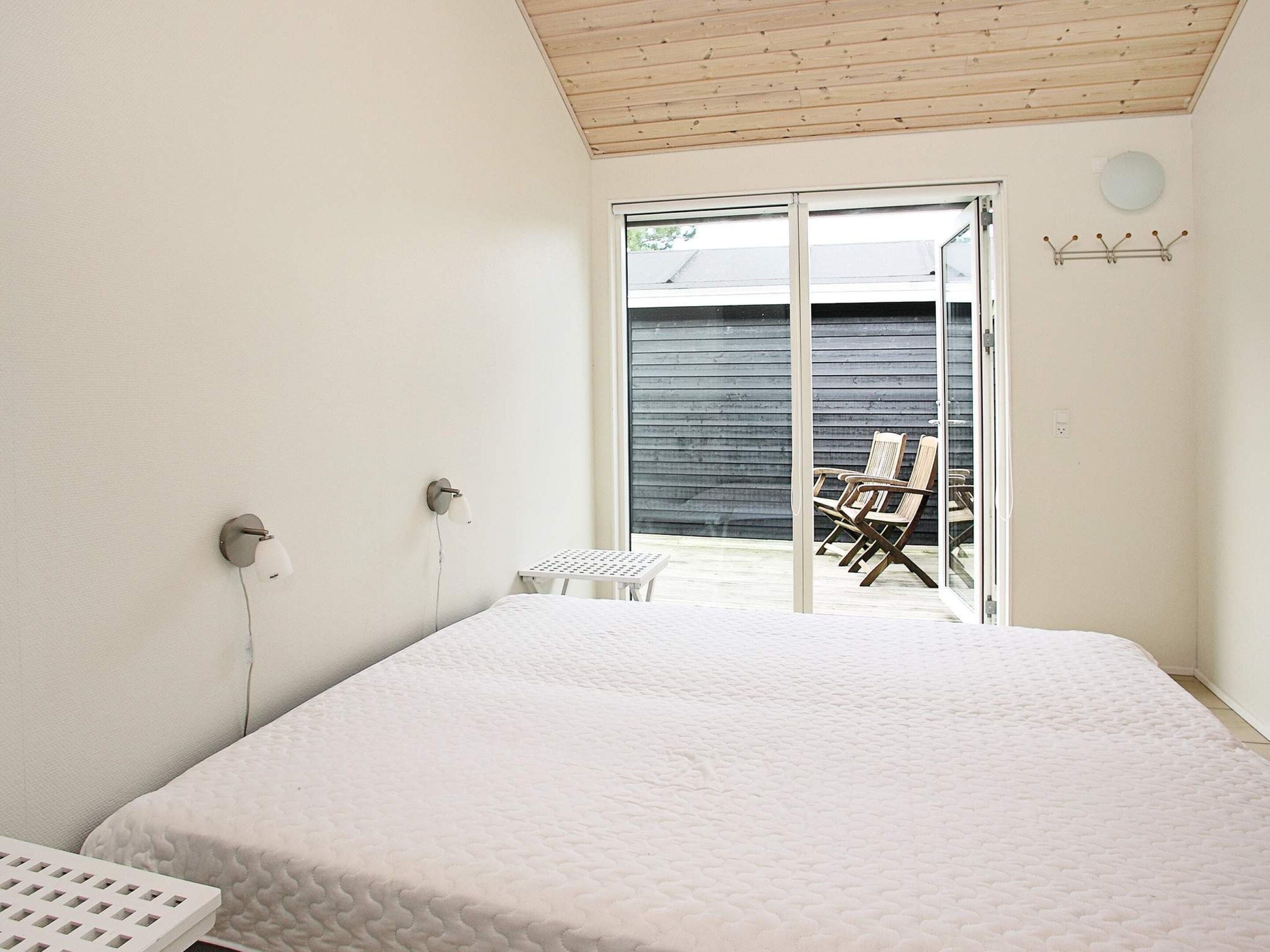 A bedroom with a bed, a small table, and a chair. There is a sliding glass door leading to an outdoor area with a table and chairs.