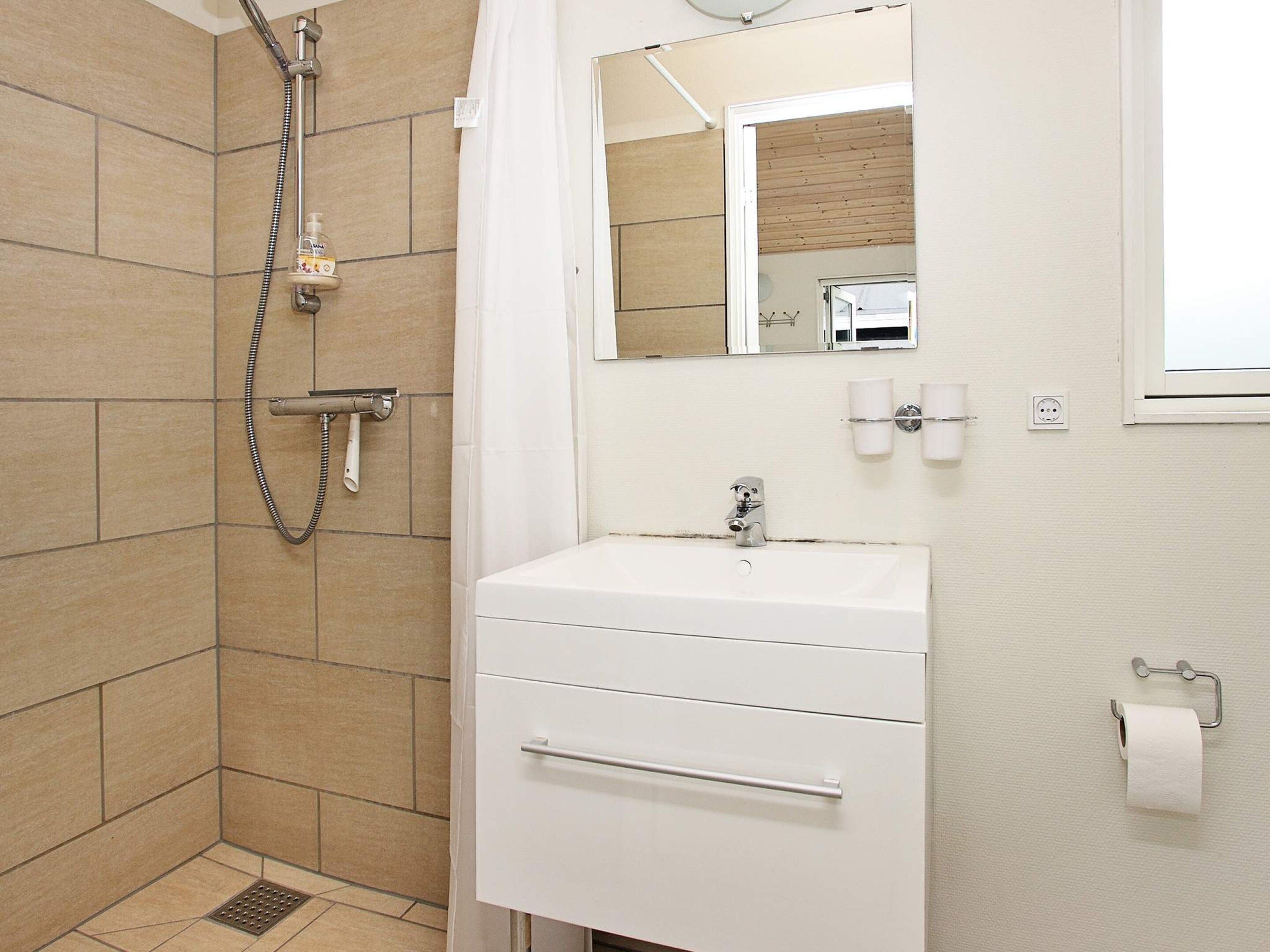 A bathroom with a shower, a sink, a mirror, and a toilet paper holder.