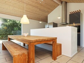 Una cocina moderna con una mesa y banco de madera, iluminación colgante y vistas al exterior.