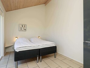 Een kleine kamer met een enkel bed, houten plafond, een wandlamp en een lijst met een afbeelding.