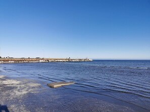 Escena costera con un rompeolas rocoso, mar tranquilo y cielo despejado.