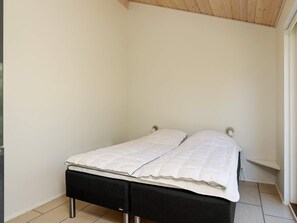 Una cama individual con estructura negra y ropa de cama blanca en una habitación con paredes blancas y techo de madera.