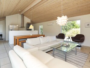 Una sala moderna con una mesa de centro de vidrio, un sofá blanco y sillones oscuros. Se ve una mesa de comedor de madera al fondo.