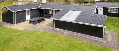 A modern house with a flat roof, a covered patio area, and a large window.