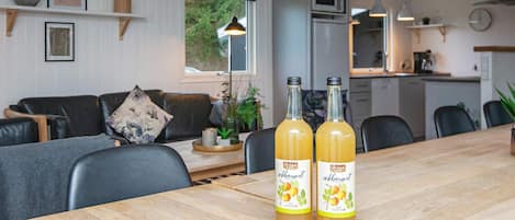 A cozy living room with a wooden dining table, two bottles of amber-colored drink, a black leather sofa, and a large window.