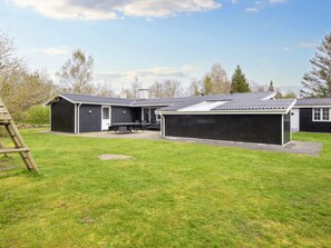 A black metal building with a covered patio area and a lawn in front.