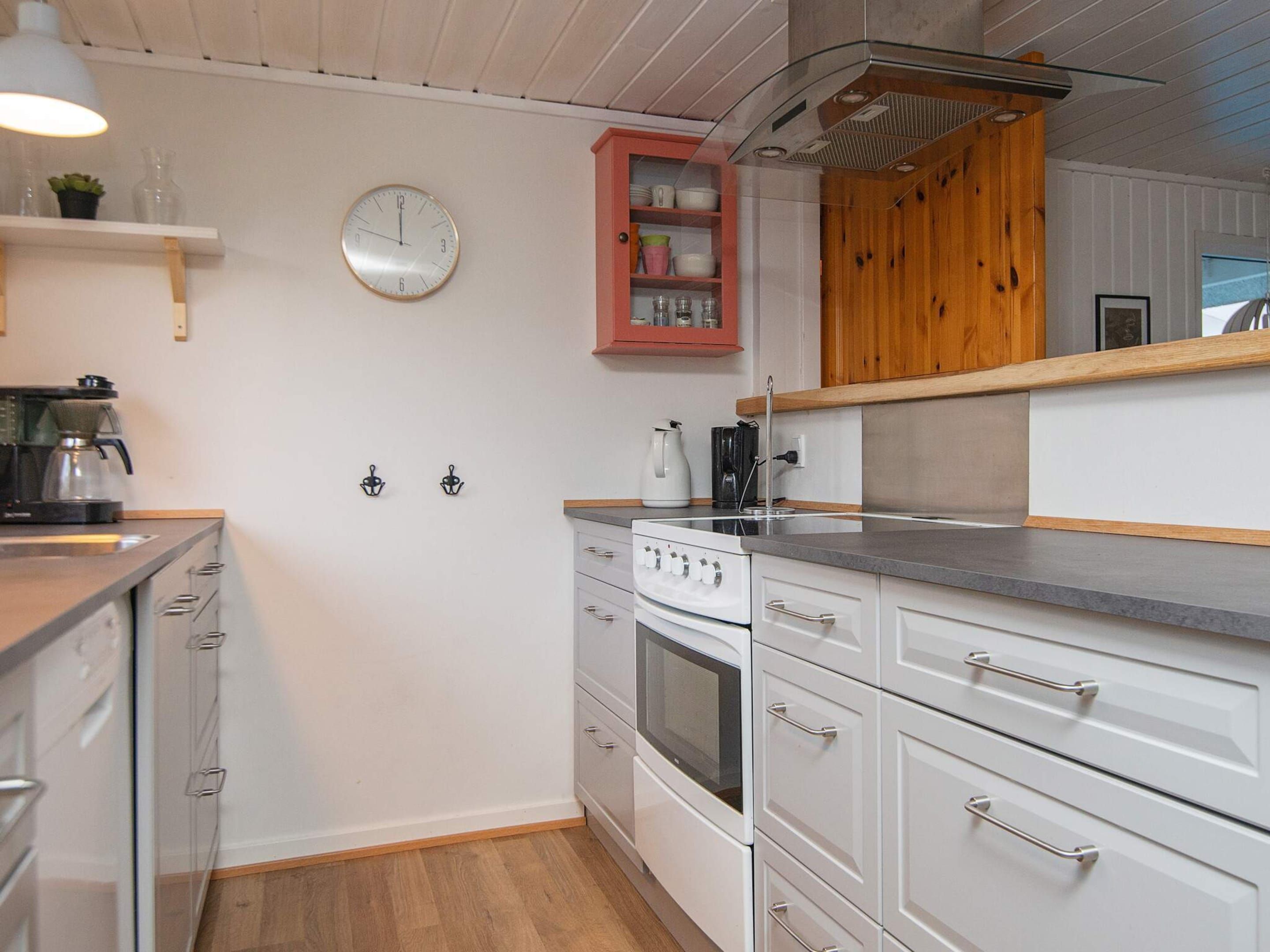 Een moderne keuken met witte kasten, een roestvrijstalen afzuigkap, een inbouwoven en een koffiezetapparaat.