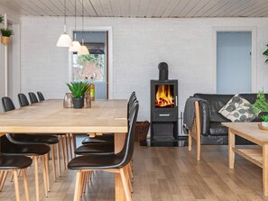 A modern living room with a central fireplace, a dining area with chairs and a table, and a sofa with a cushion.