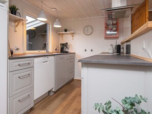 Cocina compacta con muebles blancos, encimera de madera, iluminación colgante, cafetera y un reloj en la pared.