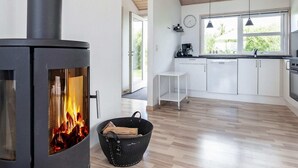 Et moderne køkken med en brændeovn, lyse skabe og et vindue med udsigt til grønne omgivelser.