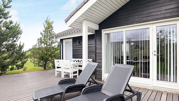 En terrasse med to liggestole og et bord, en skydedør i glas samt et hvidt gelænder.