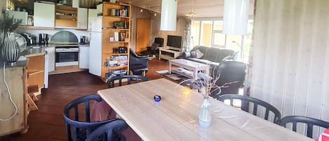 A modern kitchen with white cabinets, a dining table with chairs, and a living area with a sofa and television.