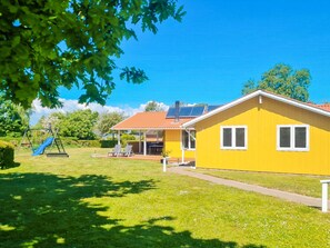 Ein gelbes Haus mit einer Terrasse, einer Schaukel und einem überdachten Außenbereich.