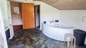 A bathroom with a large bathtub, a wooden door, and a tiled floor. - 4 Star Holiday Home in Nordborg (Nordborg)