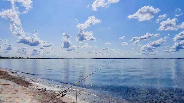 A calm lake with a fishing rod on the shore, clear sky, and scattered clouds. - 4 Star Holiday Home in Nordborg (Nordborg)
