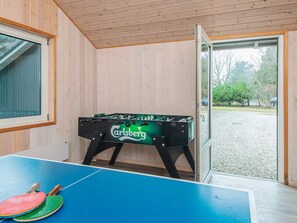 Ett rum med ett fotbollsspel, ett bordtennisbord och ett fönster med utsikt över ett grusområde och träd.