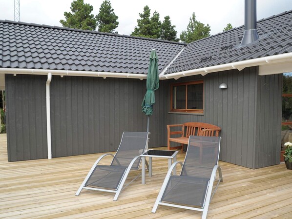 A covered outdoor area with two lounge chairs, a wooden bench, and a green umbrella.
