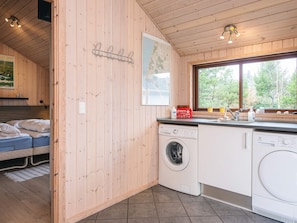 A compact room with a bed, a washing machine, a sink, and a window with a view of trees.
