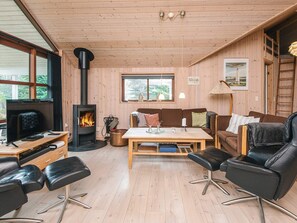 Ein gemütliches Blockhaus-Interieur mit Holzausstattung, Kamin, einer Couch, einem Couchtisch und einem Fernseher.