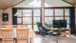 A spacious room with a large dining table, wooden chairs, a leather sofa, and a television on a wooden stand. - 4 Star Holiday Home in Blavand (Blavand)