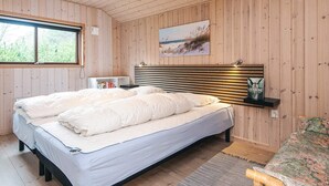 A bedroom with a bed, a bedside table, a shelf with a book, and a window.