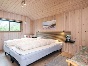 A bedroom with a bed, a bedside table, a shelf with a book, and a window.