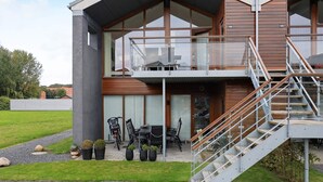 Un bâtiment moderne à deux étages, doté d’un balcon, d’un espace extérieur aménagé pour s’asseoir et d’un escalier.