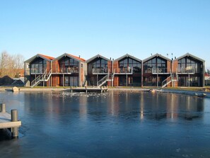 A row of modern buildings with balconies, a dock, and a calm water body in the foreground.