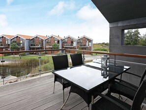 Un balcon avec une table et des chaises, donnant sur un plan d’eau et une rangée de maisons.