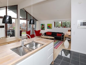 A modern kitchen with a large island, a dining area with red chairs, and a black sofa. - 4 Star Holiday Home in Bogense (Bogense)