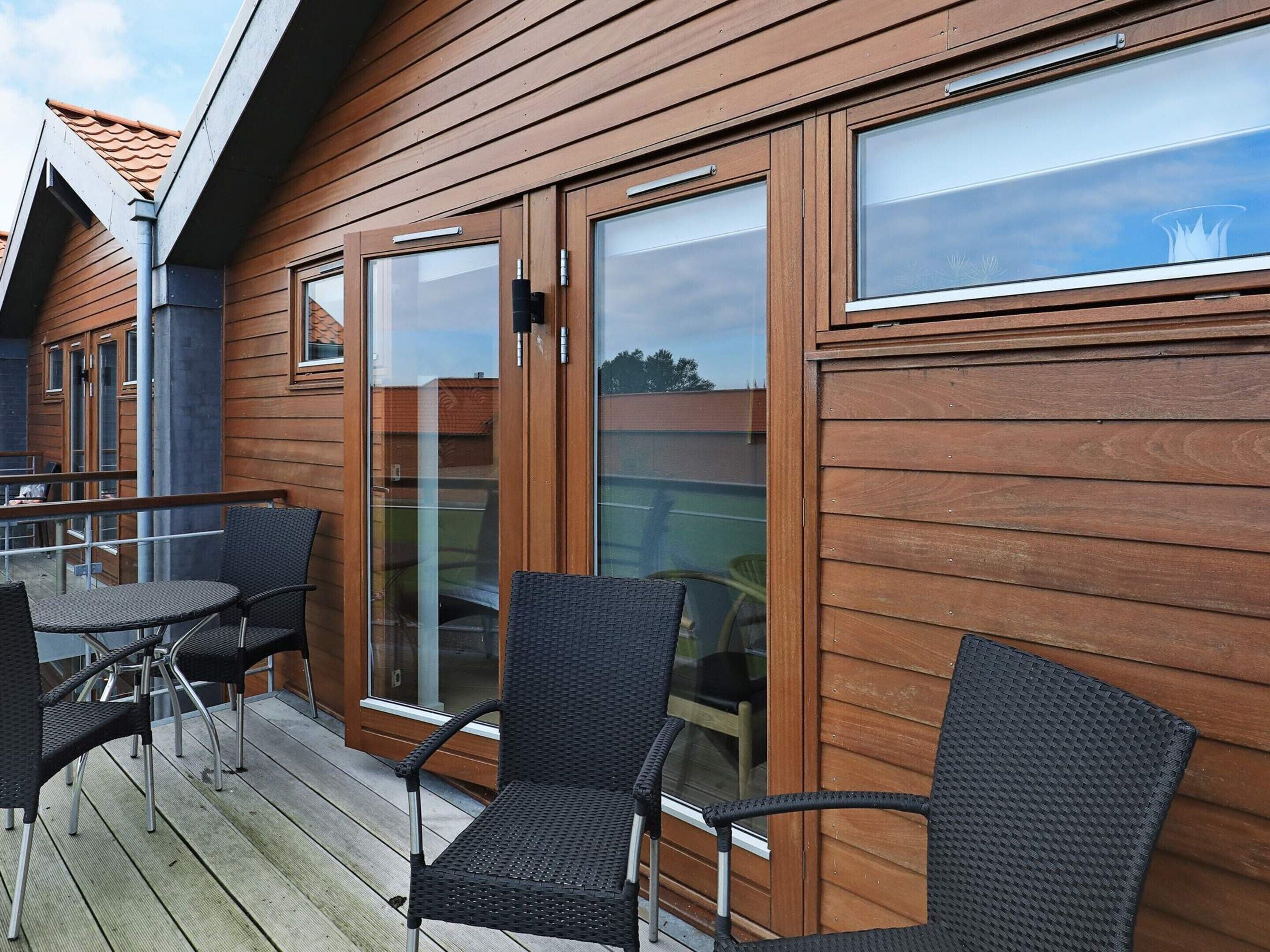 Een houten gevel met schuiframen, buiten zitplaatsen met stoelen, en een zichtbaar dakrand.