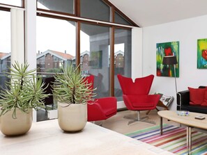 A modern living room with a large window, red chairs, and two potted plants.