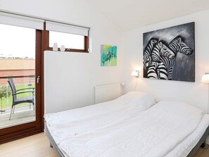 A bedroom with a bed, a window with a view of a balcony, and two wall-mounted paintings.
