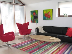 A modern living room with a black leather sofa, red chairs, a wooden coffee table, and colorful striped carpet. - 4 Star Holiday Home in Bogense (Bogense)