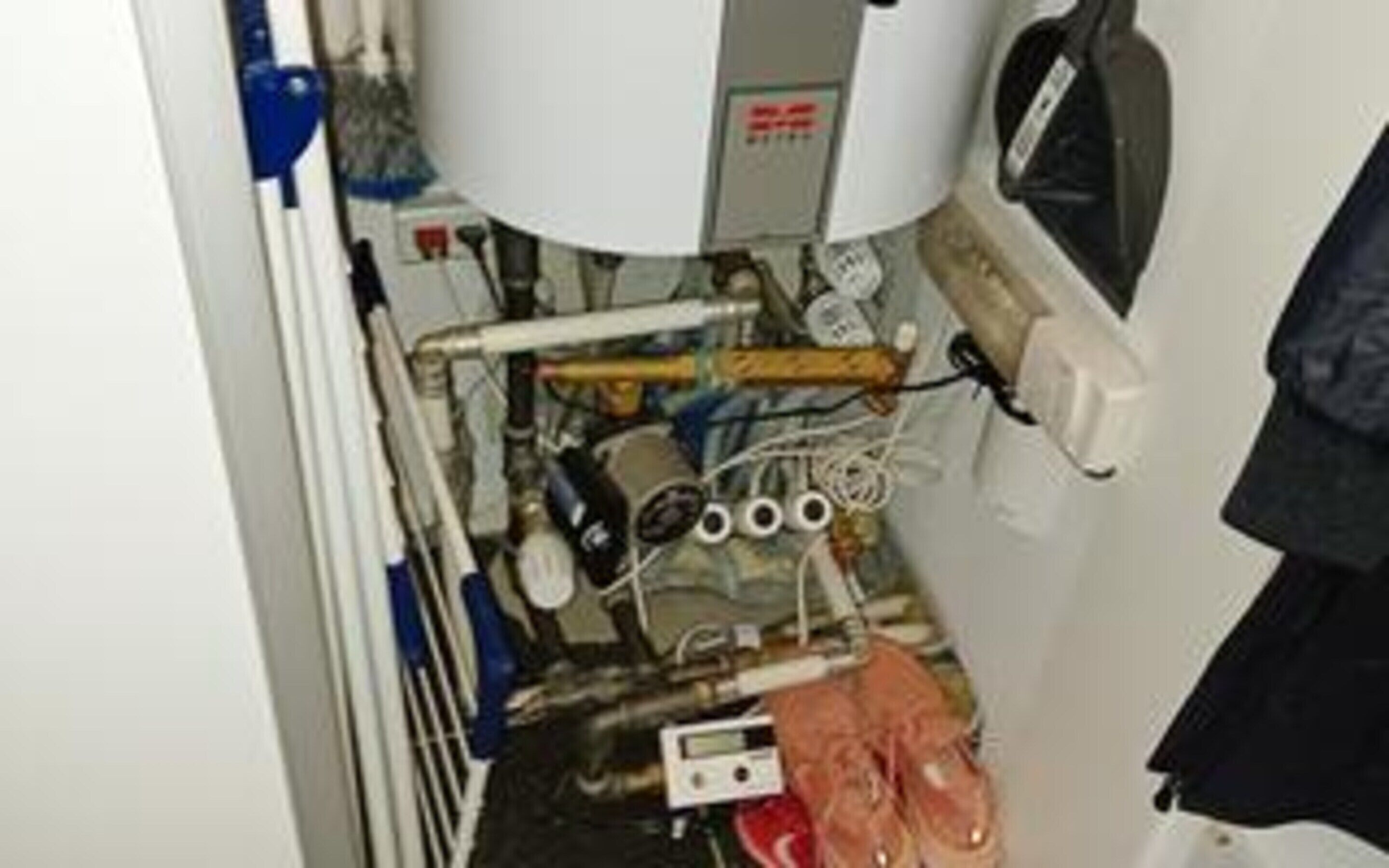 A cluttered utility area with exposed pipes, a water heater, and a control panel.