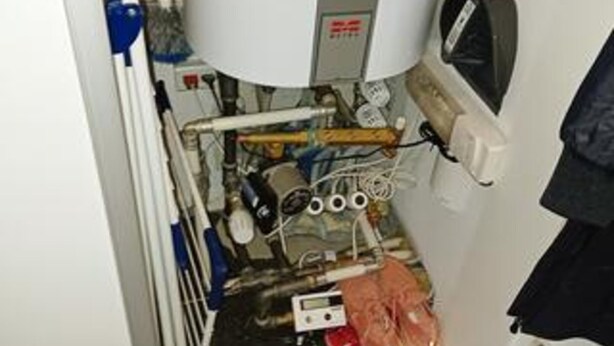 Un espace utilitaire encombré, avec des tuyaux apparents, un chauffe-eau et un panneau de commande.