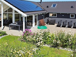 A house with a covered patio area, a garden with various flowers, and a solar panel installation on the roof. - Attractive Holiday Home in Vaggerlose near Sea (Idestrup)