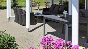 Un espace extérieur abrité, aménagé avec des meubles en osier, une table et un banc.