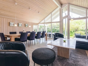 A modern interior with a wooden ceiling, large windows, a dining area with chairs, and a seating area with a sofa. - Attractive Holiday Home in Vaggerlose near Sea (Idestrup)