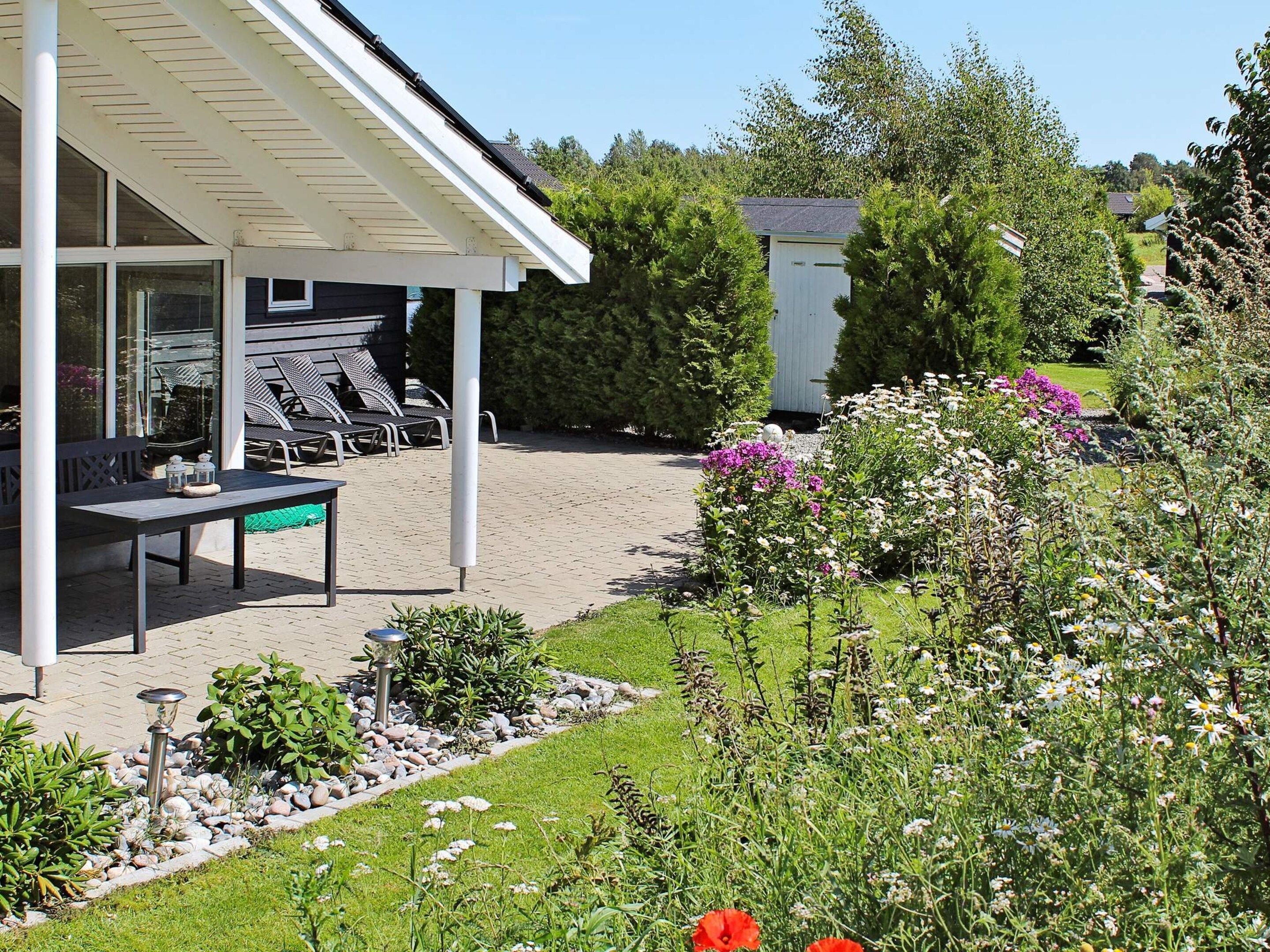 A covered outdoor seating area with a table and chairs, surrounded by a garden with various plants and flowers.