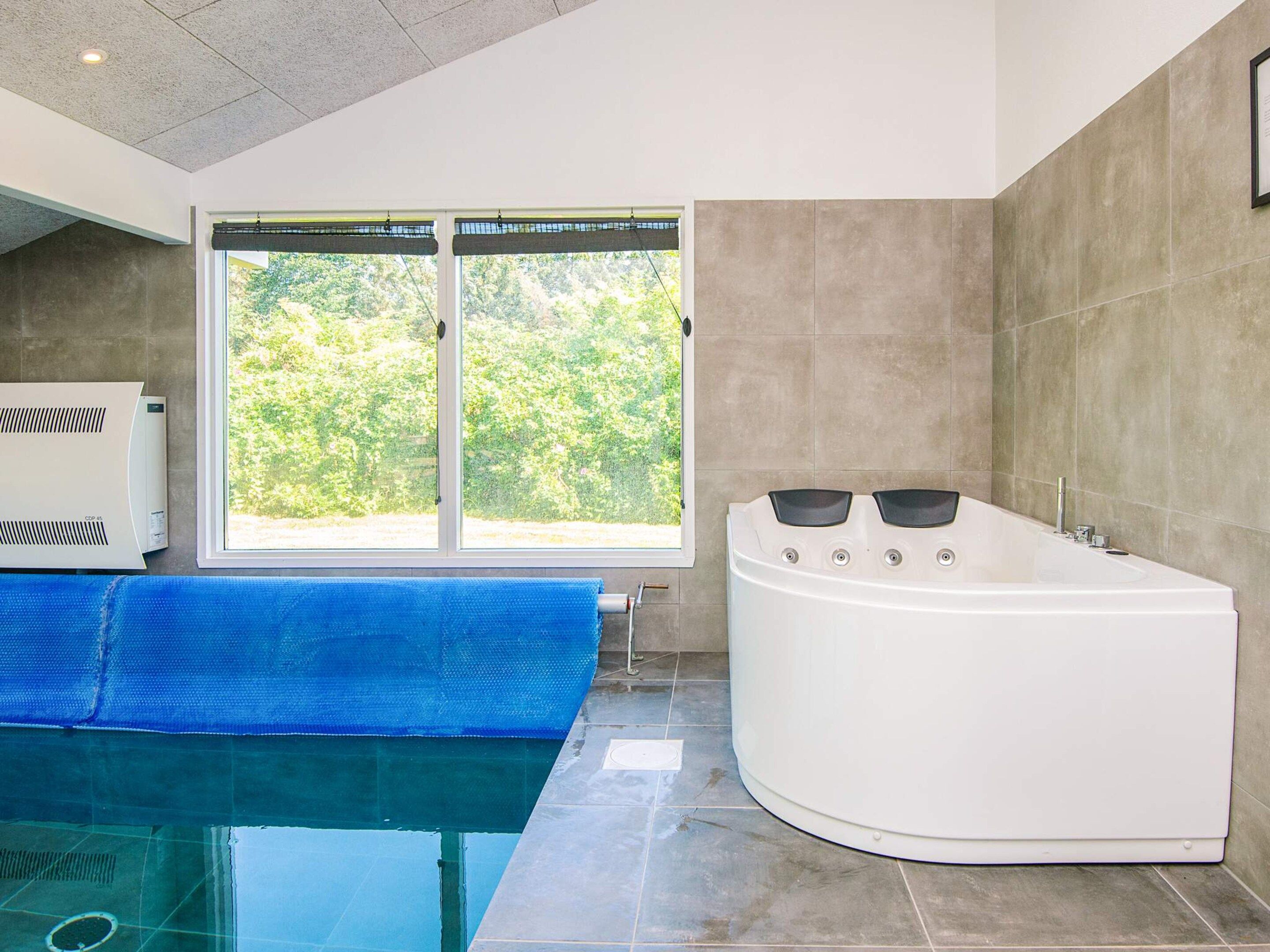 A modern bathroom with a large bathtub, a window with a view of greenery, and a blue mat on the floor.