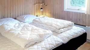 A room with wooden walls, a bed with white bedding, a bedside lamp, and a window with a view of trees.