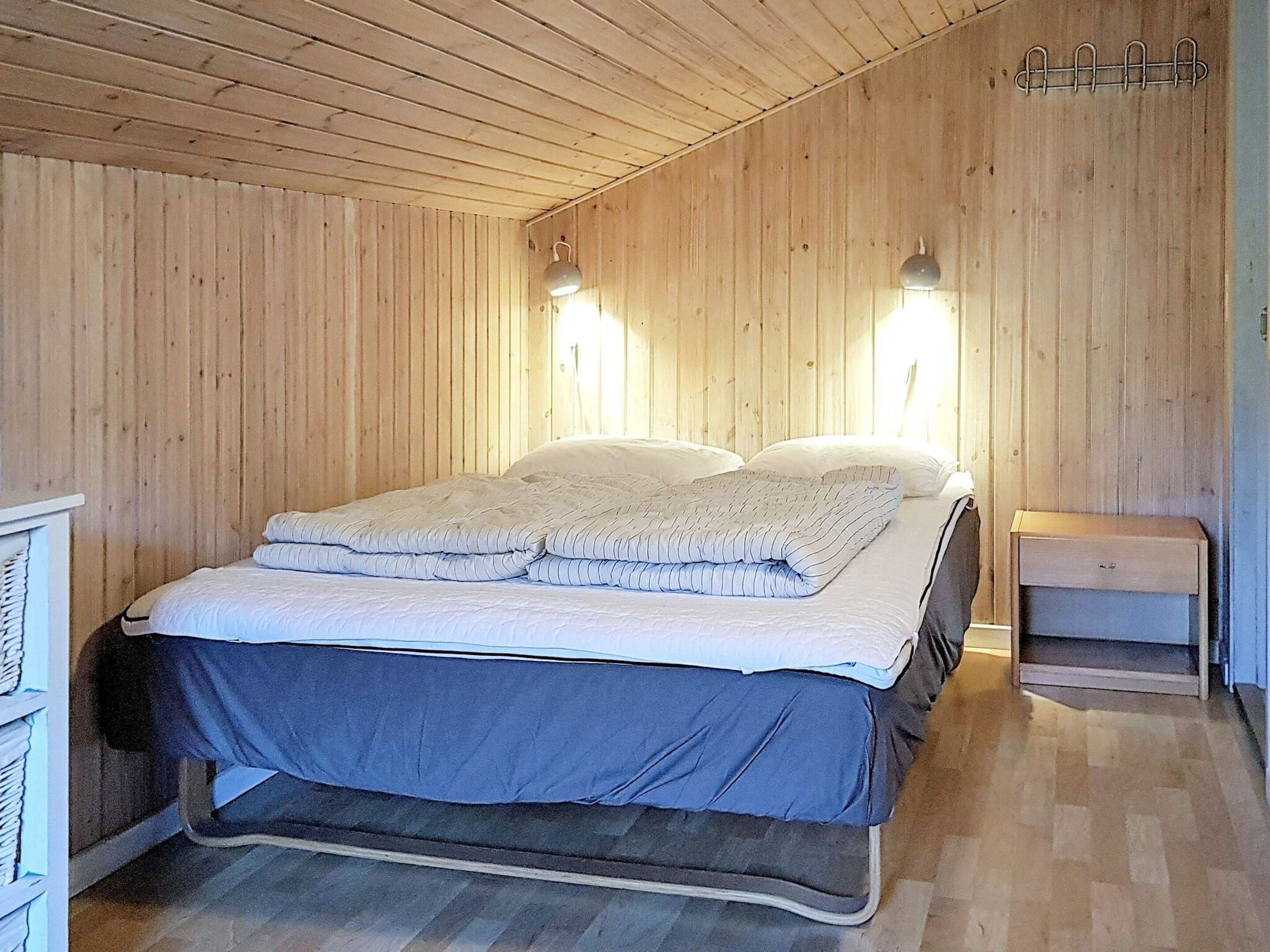 Une pièce avec un lit, des murs en bois et deux lampes fixées au mur.