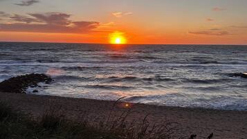 A sunset over the ocean with waves crashing onto a rocky shore.
