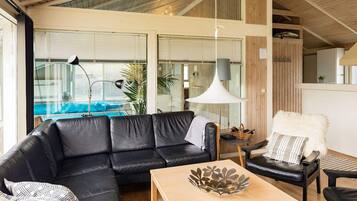 Una sala de estar moderna con un sofá de cuero negro, una mesa de centro de madera y vista a una piscina a través de amplios ventanales.