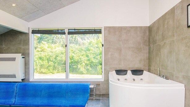 A modern bathroom with a glass-enclosed pool, a large bathtub, and a view of greenery through a window.