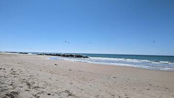 A beach with footprints, waves, and birds.