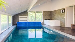 An indoor swimming pool with a blue bench, a white spa area, and large windows allowing natural light.
